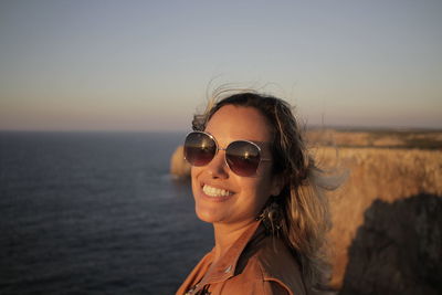 Portrait of smiling young woman wearing sunglasses against sky during sunset