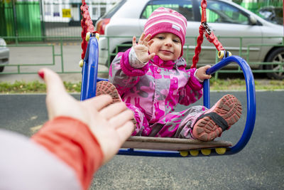 Cropped hand of mother giving high five to daughter siting on swing