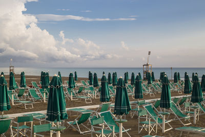 Parasols and deck chairs at beach against sky