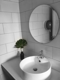 Monstera palm leaves in a vase near modern white brick wall in bathroom.