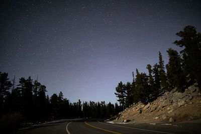 Empty road amidst trees against sky at night