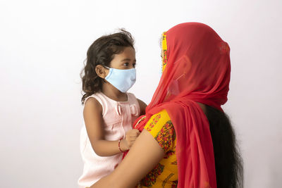 Cute girl wearing flu mask with mother against white background