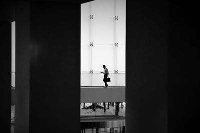 Man walking on elevated walkway by building seen through doorway