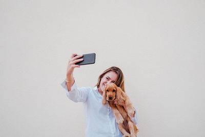 Woman photographing with mobile phone against wall