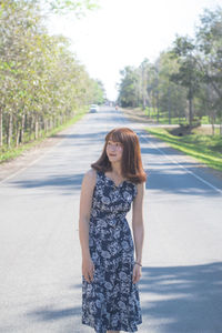 Portrait of smiling young woman on road against trees