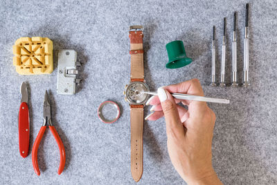 Cropped hand of woman repairing wristwatch with tools on table