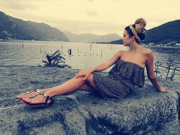 Full length of woman relaxing on rock against sea and sky