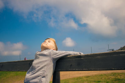 Boy leaning on railing against sky
