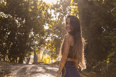 Rear view portrait of smiling woman standing in public park