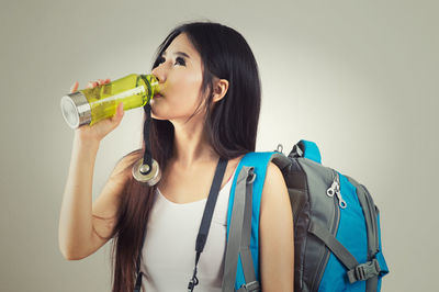 Portrait of young woman drinking water from bottle against gray background