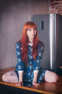 Portrait of woman wearing blue dress sitting on wooden table at home