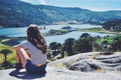 Rear view of woman sitting by lake against mountains