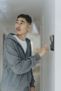 Teenage boy using digital tablet mounted on wall while standing at smart home