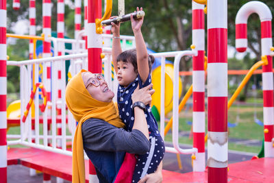 Mother assisting daughter in hanging on monkey bars at playground