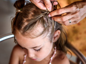 Cropped hands of mother braiding daughter hair