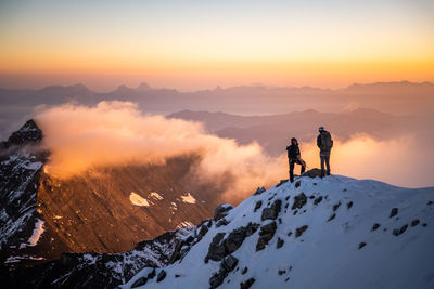 People standing on snowcapped mountain against sky during sunrise
