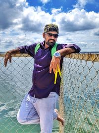 Portrait of man standing against fence at lakeshore