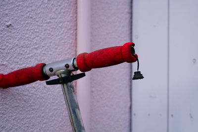 Close-up of handlebar of red push scooter against wall