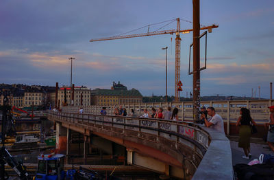 People on bridge against sky at sunset