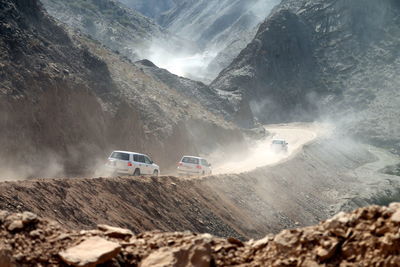 Cars moving on dirt road by mountains