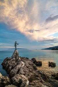 Statue on rock by sea against sky