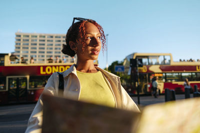 Thoughtful young woman wearing sunglasses holding map