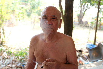 Shirtless senior man smoking cigarette while sitting outdoors