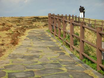 Man standing on railing against sky