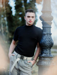 Portrait of young man standing by pole