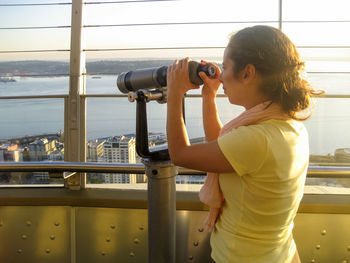 Young woman looking through coin-operated binoculars by river