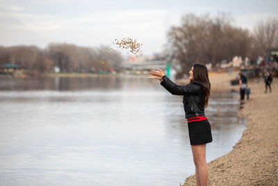 An attractive beautiful girl standing on the lake bank and throwing stones into the water.