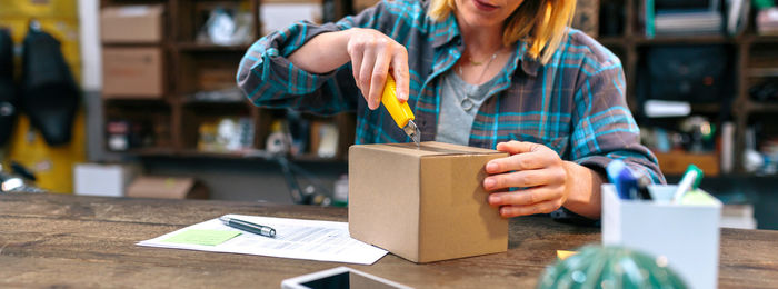 Banner of unrecognizable woman opening box with cutter. parcel delivery and ecommerce concept.