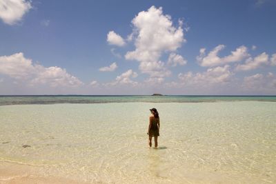 Rear view of woman standing on beach against sky