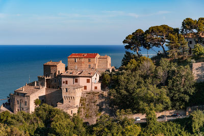 Trees and buildings by sea against sky