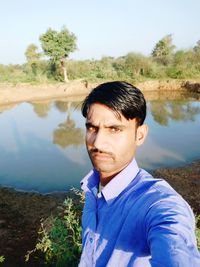 Portrait of man standing by lake against trees