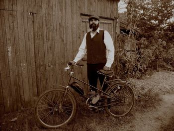 Portrait of young man with bicycle standing on field against wall