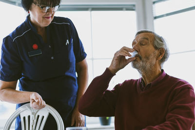 Caretaker looking at senior man taking medicine