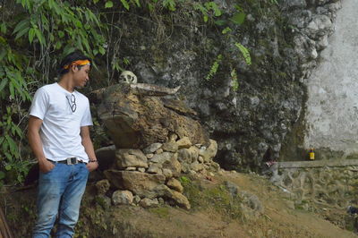 Young man looking away while standing by rock