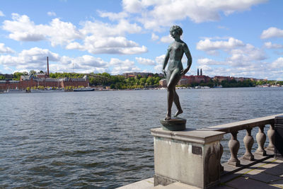 Statue by river in city against sky