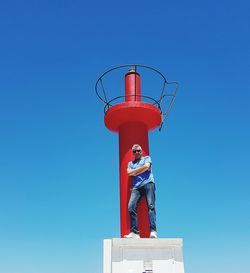 Low angle view of red  lighthouse against clear blue sky an one man in front