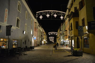 People walking on illuminated street amidst buildings at night