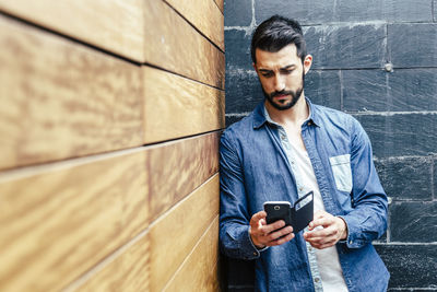 Young man using mobile phone while standing on wall