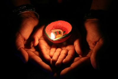 Cropped hands of mother and child holding lit diya in darkroom