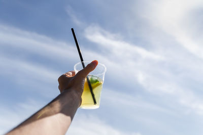Cropped hand of woman holding thermometer against sky