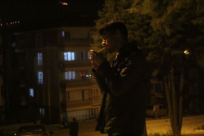 Side view of young man drinking glass at night