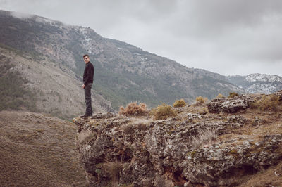 Man standing on cliff by mountain