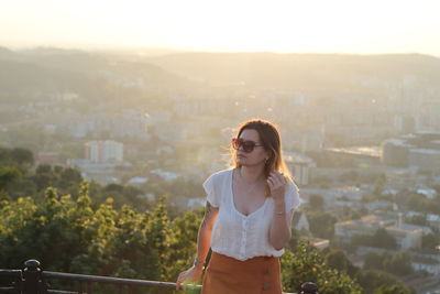 Young woman wearing sunglasses standing against cityscape in city