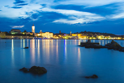 Illuminated buildings by sea against sky
