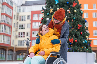 Caucasian woman driving her friend in a wheelchair by the christmas tree