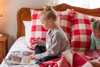 Cute girl drawing in book while sitting on bed at home